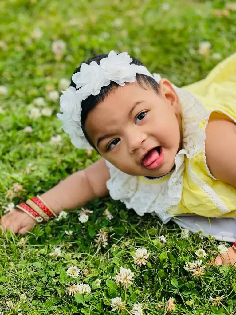 A child in a yellow outfit and white flower headband resting on grass