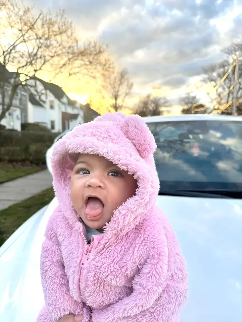 A child in a soft pink hooded coat outdoors at sunset