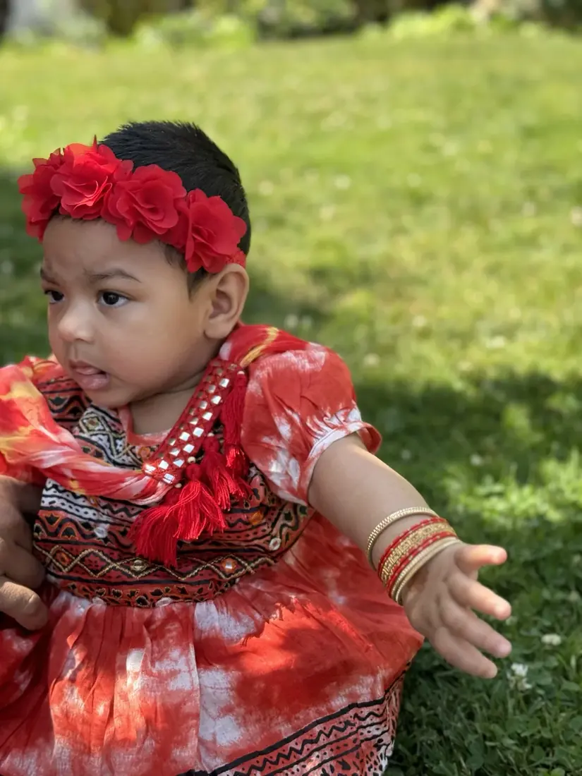A child in a red traditional outfit and flower headband outdoors